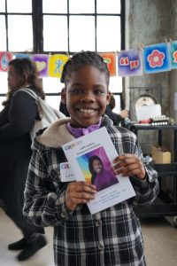 Student faces camera, smiling, holding the exhibition booklet in her hands that bears her self-portrait